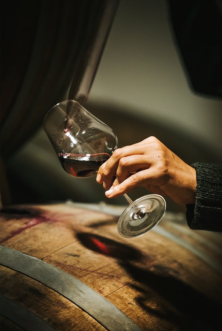 Mano sujetando copa de vino, sirviendo un Vino Tinto directo de la barrica
